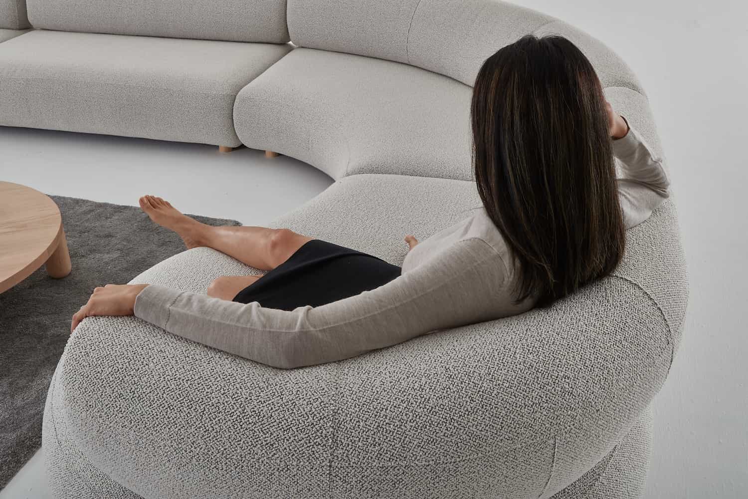 Woman sitting at the Eclipse modular sofa curved end with her back to us.