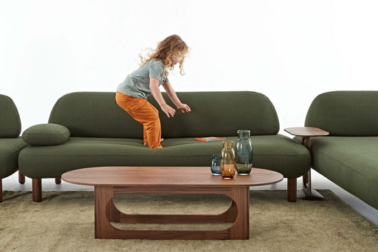 Child standing on the sturdy Ethos Plus green sofa reaching for a book.