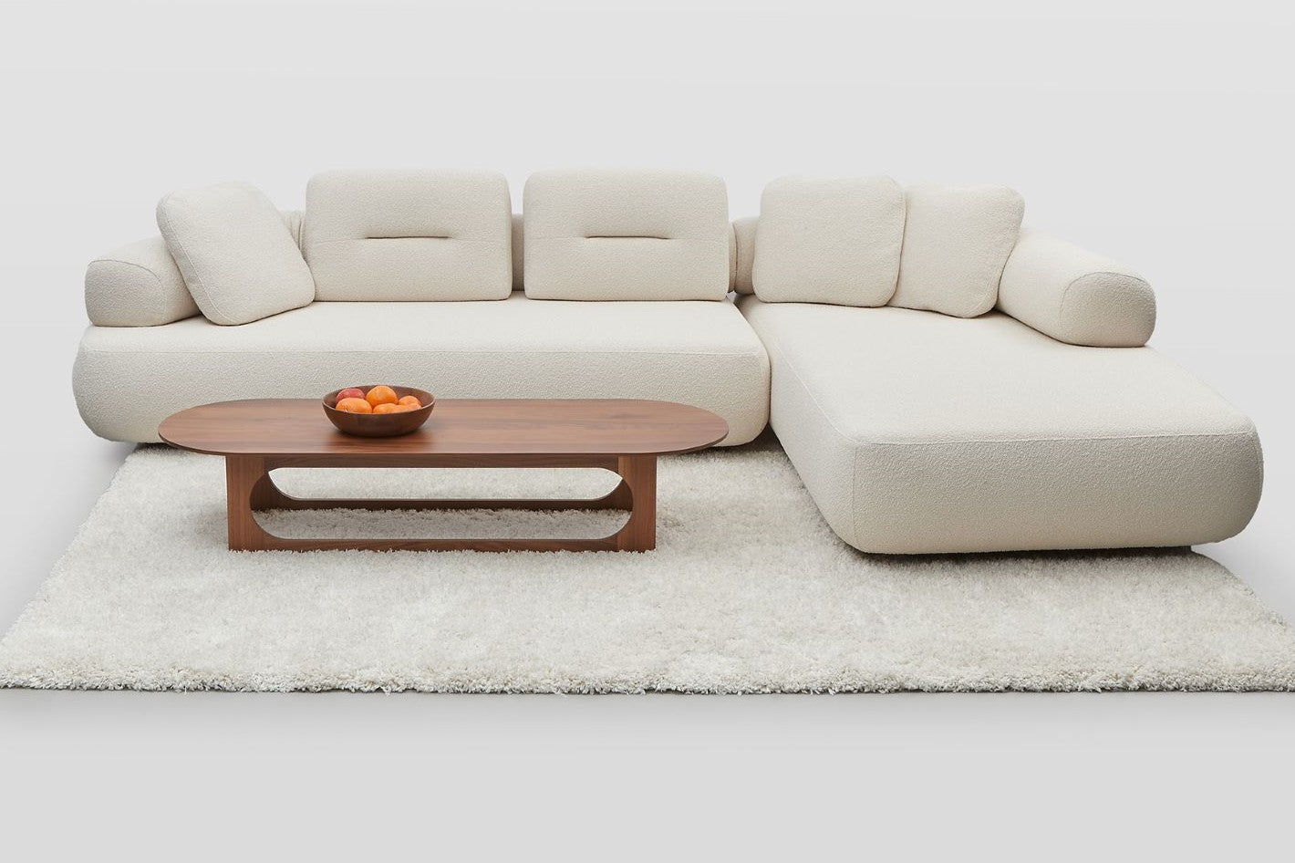 Newman L-shaped sofa and chaise set in white boucle with Ethos table and bowl of oranges on a white rug.