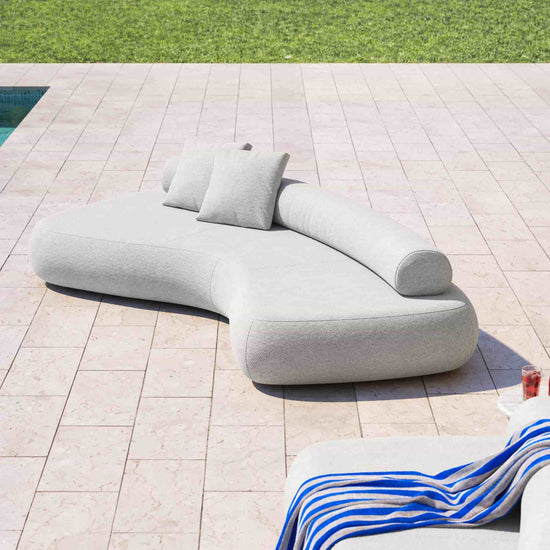 3 metre Rolly outdoor sofa shown on travertine tiles beside a pool with grass in background.