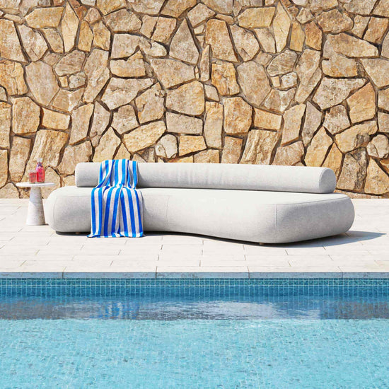 A 3 1/2 metre Rolly Outdoor Sofa shown next to a pool and in front of a sandstone wall.