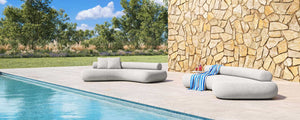 Two outdoor Rolly sofas by E9Design in a backyard setting by a pool with travertine tiles and sandstone wall.