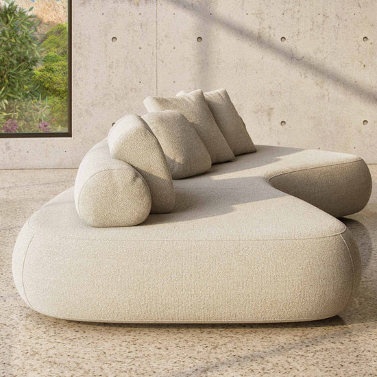 The Rolly designer sofa in Entwine fabric shown from the side with its back roll and cushions on a terrazzo floor with concrete walls.